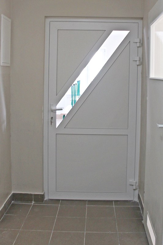 Obrazek przedstawia zdjęcie korytarza i zamkniętych drzwi ze skośnym okienkiem