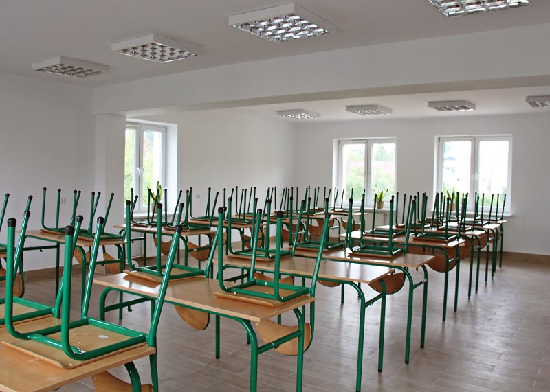 Obrazek przedstawia zdjęcie klasy z biurkami na których stoją odwrócone krzesła