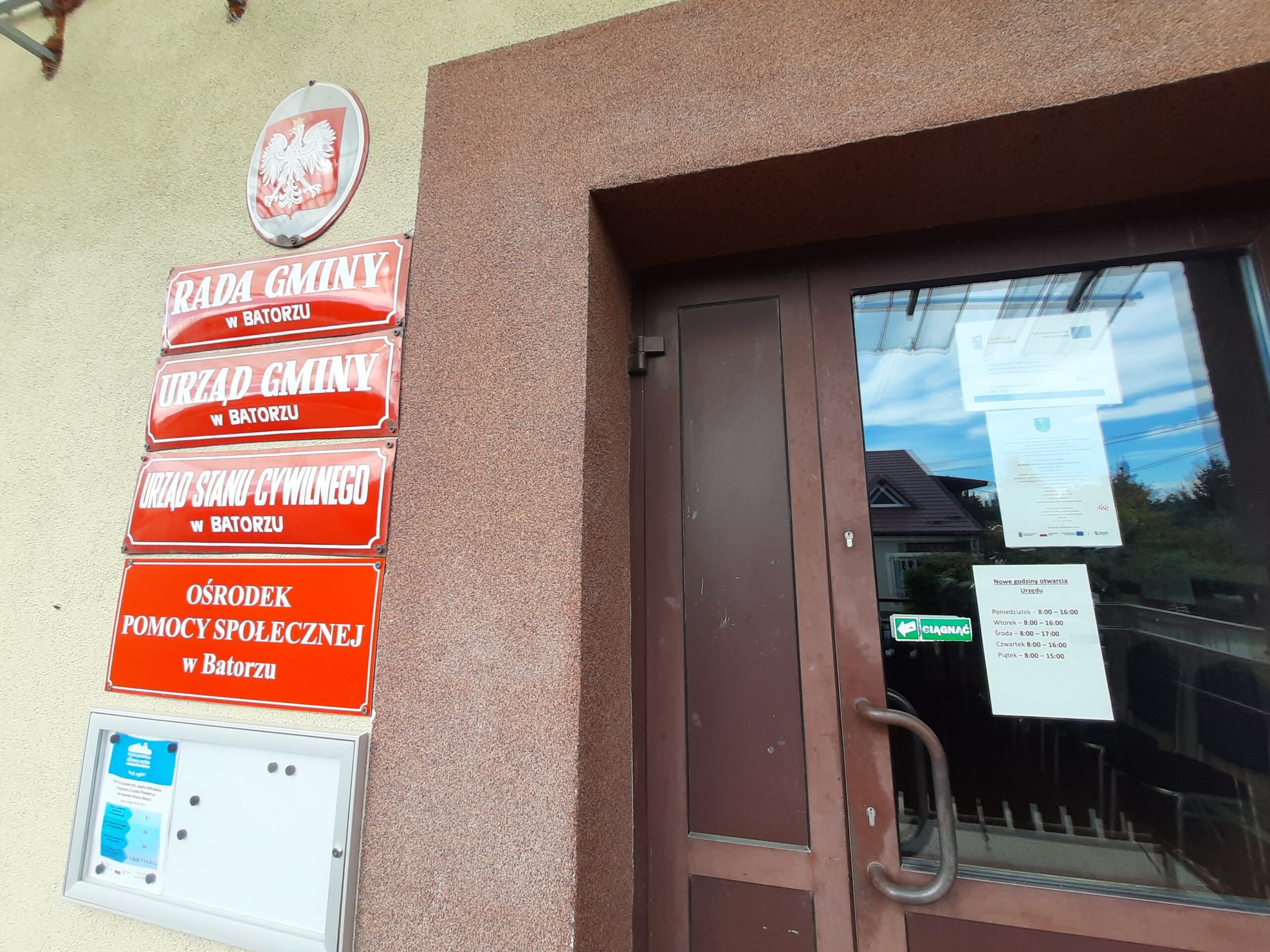 Plakat – Powiat Janowski realizuje projekt: System doradztwa sprzyjający osiągnieciu neutralności klimatycznej w Powiecie Janowskim wraz z zaproszeniem na bezpłatne konsultacje wywieszony na drzwiach wejściowych budynku Urzędu Gminy Batorz