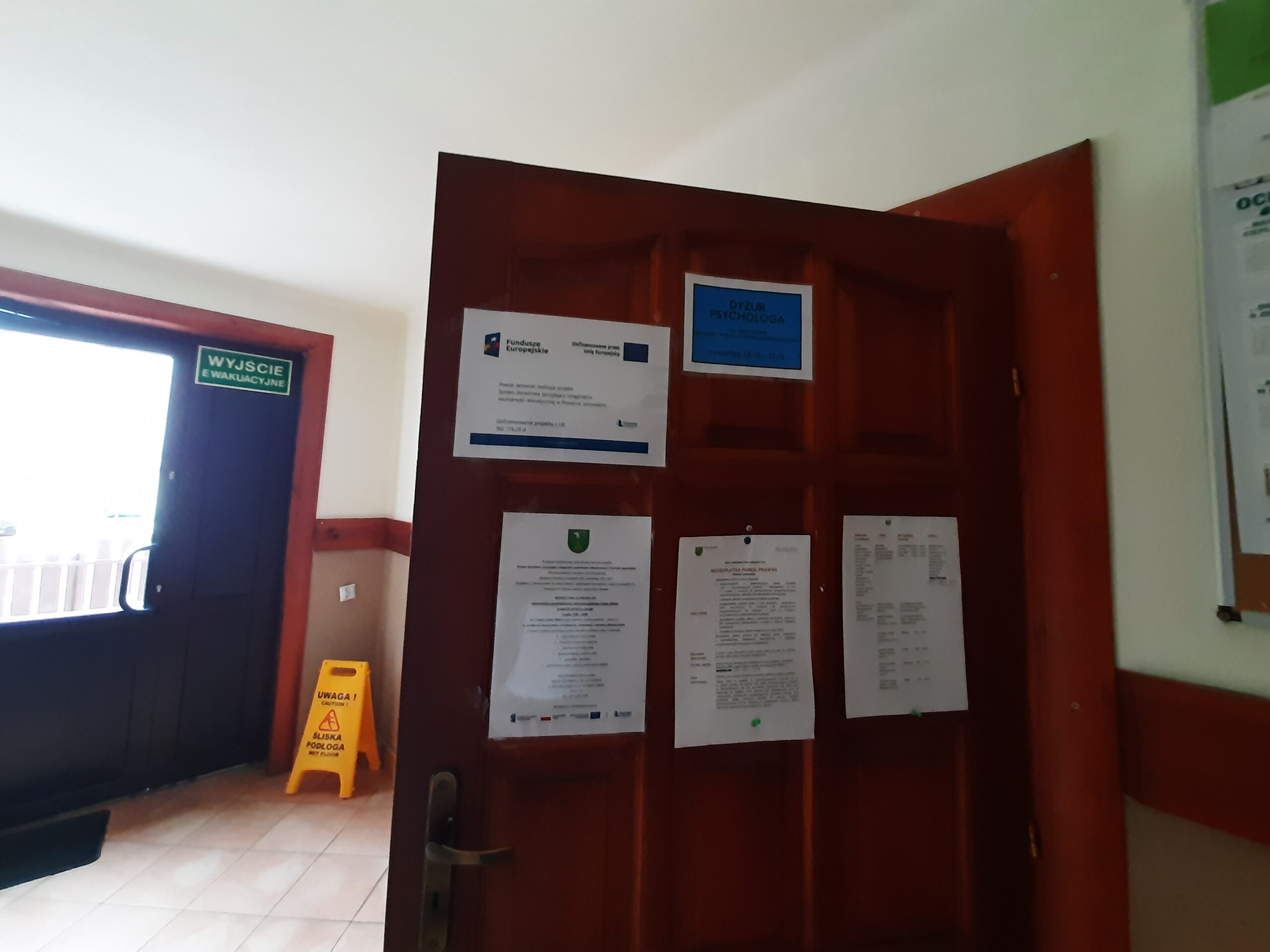 Otwarte drzwi sali narad Urzędu Gminy Batorz z wywieszonym na drzwiach plakatem Powiat Janowski realizuje projekt: System doradztwa sprzyjający osiągnieciu neutralności klimatycznej w Powiecie Janowskim wraz z zaproszeniem na bezpłatne konsultacje
