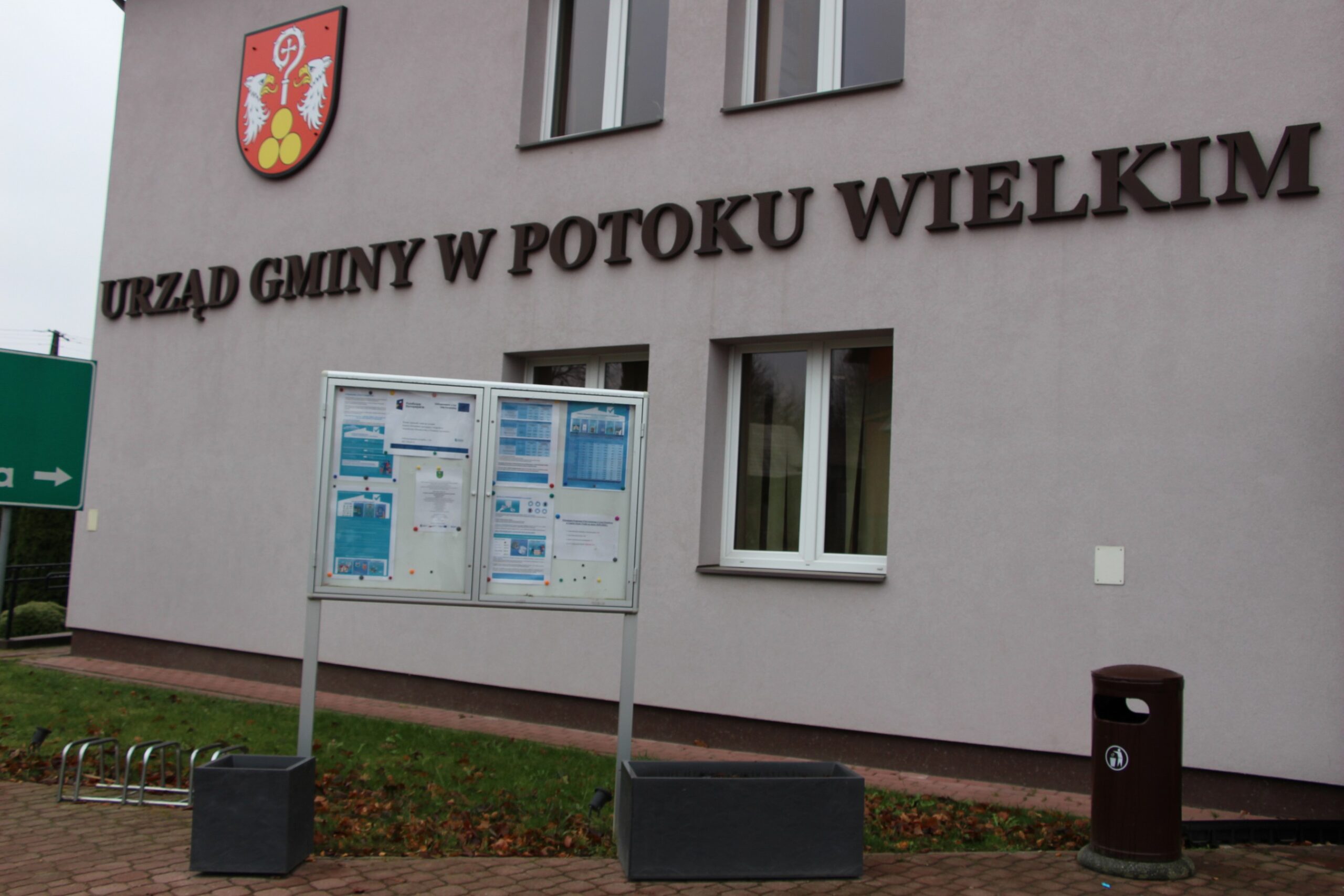 Plakat – Powiat Janowski realizuje projekt: System doradztwa sprzyjający osiągnięciu neutralności klimatycznej w Powiecie Janowskim wraz z zaproszeniem na bezpłatne konsultacje wywieszony na tablicy ogłoszeń przed budynkiem Urzędu Gminy Potok Wielki