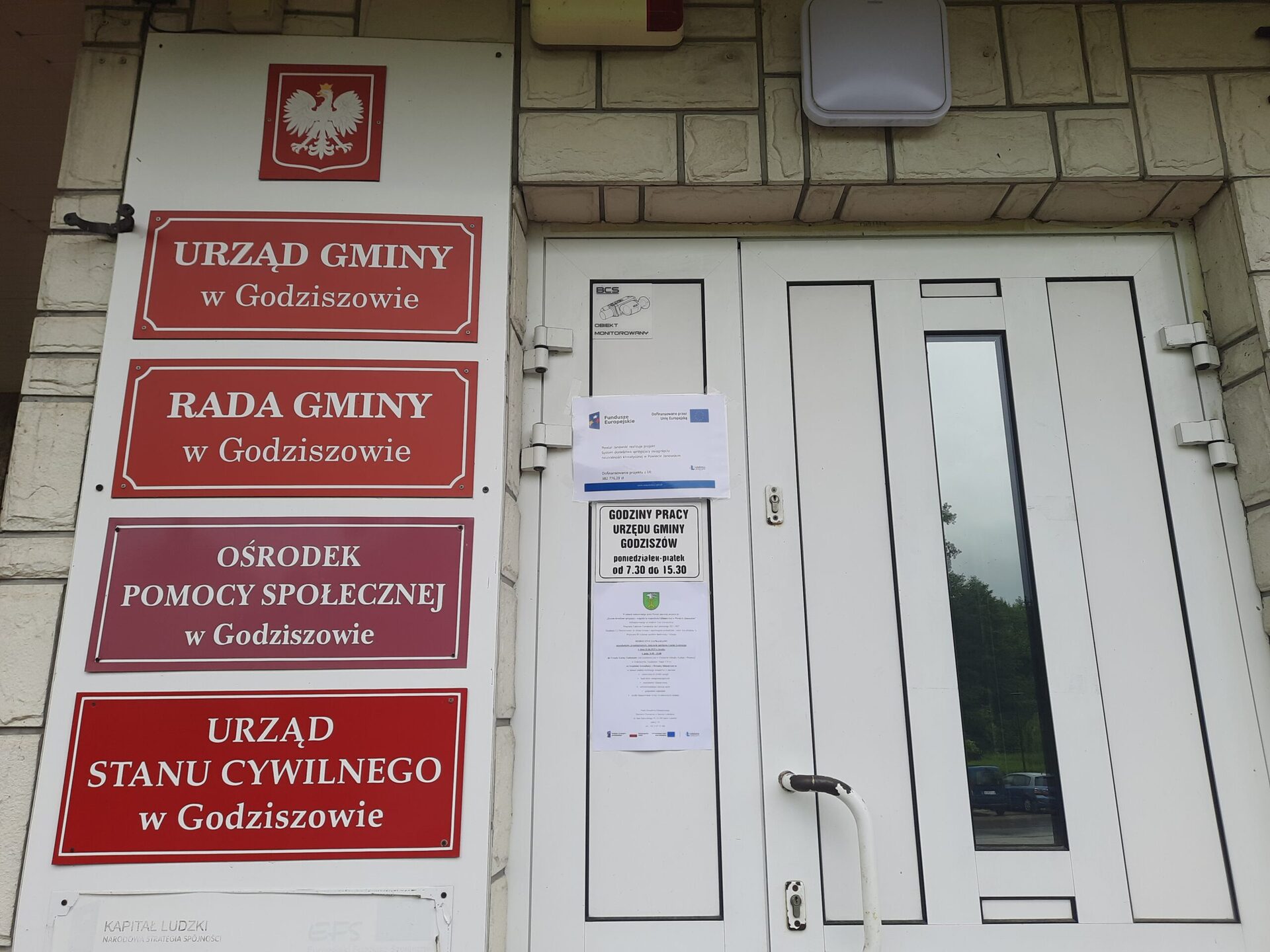 Plakat - Powiat Janowski realizuje projekt: System doradztwa sprzyjający
osiągnięciu neutralności klimatycznej w Powiecie Janowskim wraz z zaproszeniem na
bezpłatne konsultacje wywieszony na drzwiach wejściowych budynku Urzędu Gminy
Godziszów