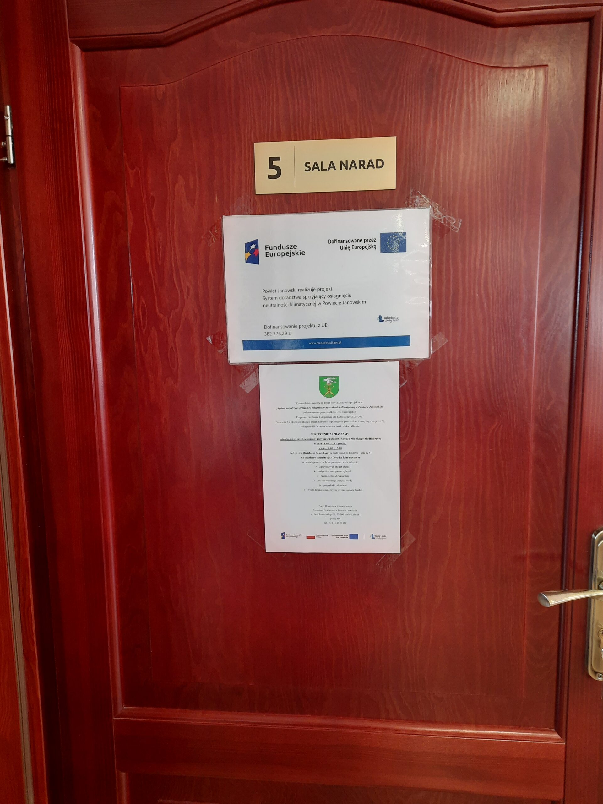 Plakat - Powiat Janowski realizuje projekt: System doradztwa sprzyjający osiągnięciu neutralności klimatycznej w Powiecie Janowskim wraz z zaproszeniem na bezpłatne konsultacje wywieszony na  drzwiach sali narad Urzędu Miejskiego Modliborzyce