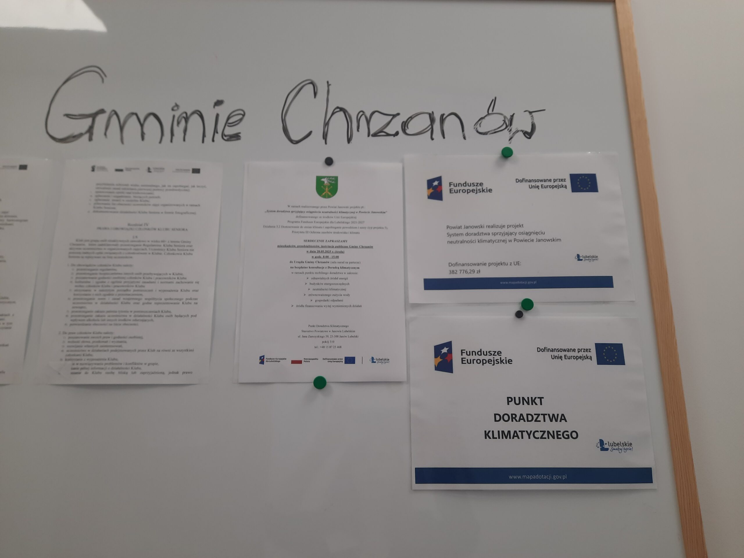 Plakat - Powiat Janowski realizuje projekt: System doradztwa sprzyjający osiągnieciu neutralności klimatycznej w Powiecie Janowskim wraz plakatem Doradztwa Klimatycznego oraz zaproszeniem na bezpłatne konsultacje wywieszony na tablicy ogłoszeń przed salą narad w Urzędzie Gminy Chrzanów