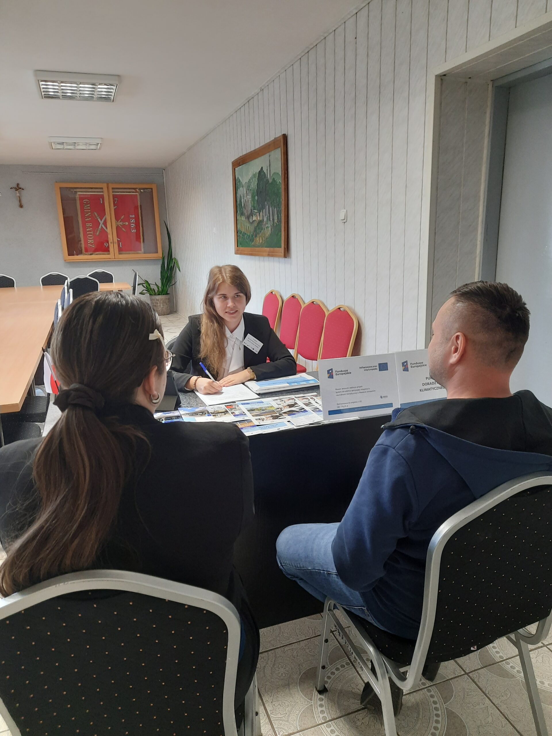 Doradca klimatyczny wraz z interesantami udzielający bezpłatnych konsultacji w zakresie neutralności klimatycznej wraz z uzupełnianiem kart doradztwa w sali narad podczas realizacji Mobilnego Punktu Doradztwa Klimatycznego w Urzędzie Gminy Batorz w dniu 21 maj 2025 r.