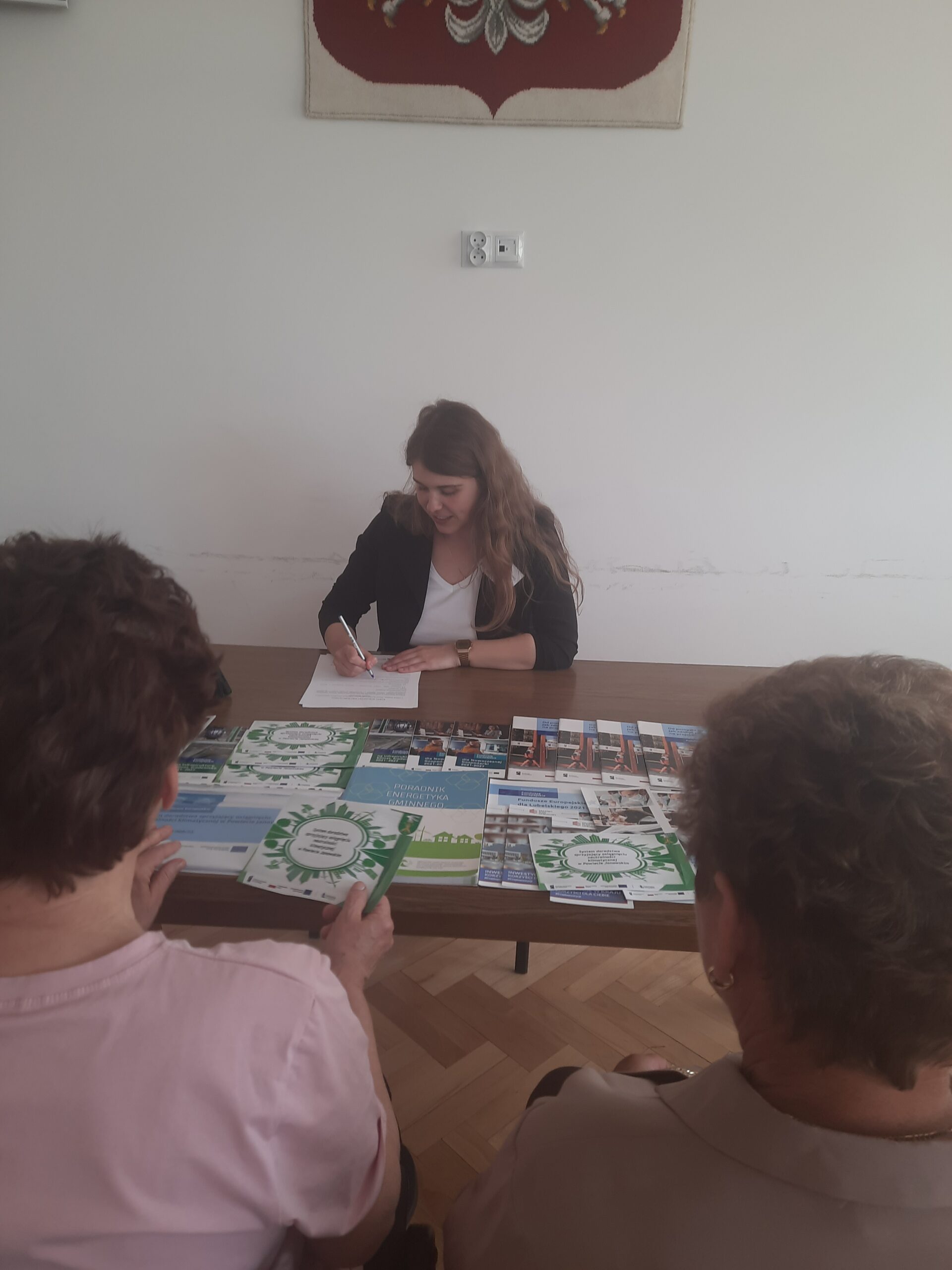 Doradca klimatyczny wraz z interesantami udzielający bezpłatnych konsultacji w zakresie neutralności klimatycznej wraz z uzupełnianiem kart doradztwa w sali narad podczas realizacji Mobilnego Punktu Doradztwa Klimatycznego w Urzędzie Gminy Chrzanów w dniu 28 maj 2025 r. w przybliżeniu