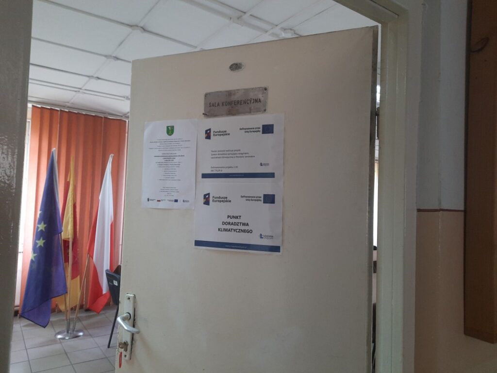 Zdjęcie 3: Plakat - Powiat Janowski realizuje projekt: System doradztwa sprzyjający osiągnięciu neutralności klimatycznej w Powiecie Janowskim wraz plakatem Doradztwa klimatycznego oraz zaproszeniem na bezpłatne konsultacje wywieszony na drzwiach sali narad Urzędu Gminy Dzwola